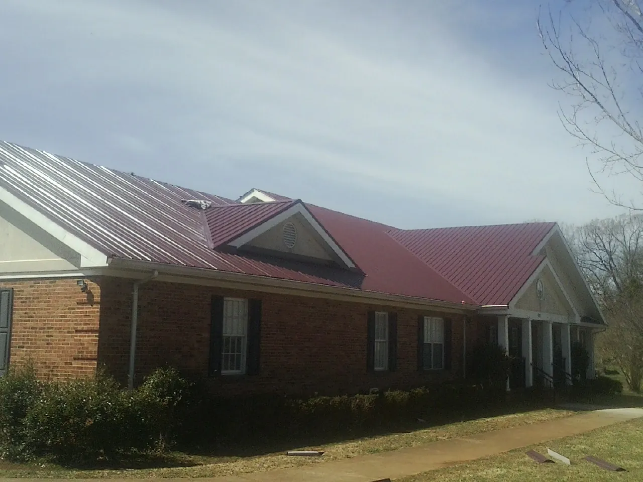 Red metal roof with gabled entries on a long brick building, from a Hail Damage Roof Repair job in Cave Creek